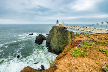Dramatic coastal view of Point Bonita Lighthouse on a rocky cliff with a suspension bridge and...