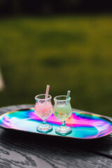 Two refreshing cool and funky cocktails with straws on a colorful, reflective tray. Summer...