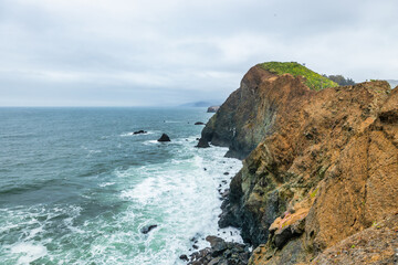 Dramatic coastal view of Point Bonita Lighthouse on a rocky cliff with a suspension bridge and powerful ocean waves, Marin Headlands, California