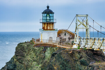 Dramatic coastal view of Point Bonita Lighthouse on a rocky cliff with a suspension bridge and...