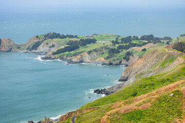 Fototapeta premium Scenic panoramic view of Marin Headlands with winding road, lush green hills, and Pacific Ocean coastline on a clear spring day, California nature landscape