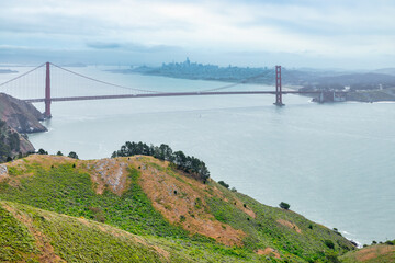 Iconic view of the Golden Gate Bridge stretching across the blue waters of the San Francisco Bay, seen from a green cliffside near Kirby Cove. A timeless symbol of California travel and nature