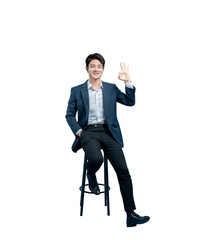 young Asian professional sitting on a stool makes an 'OK' hand gesture, signifying approval,...