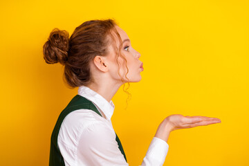 Charming young woman in a white shirt blowing a kiss on a vibrant yellow background promoting...