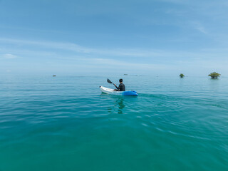 A man paddles a kayak on a tropical island. A man enjoying a sunny day while kayaking
