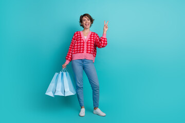 Full length photo of cheerful positive lady wear pink cardigan showing v-sign holding shoppers...