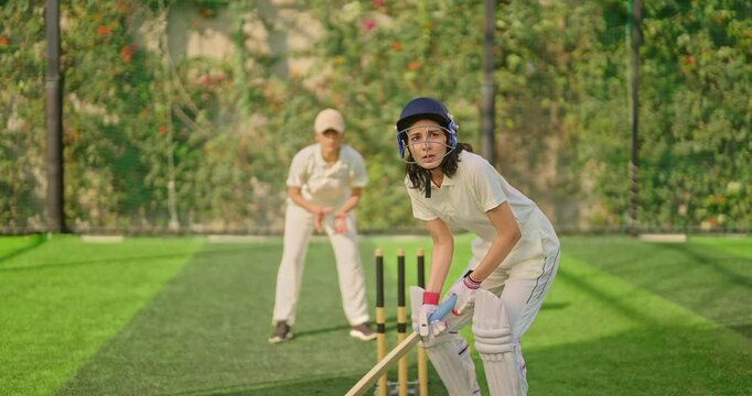 Indian gen z young adult athlete sports woman girl standing at outdoor match play ground wear gloves white uniform protective helmet Asian cricket player female lady hold bat hitting ball do practice