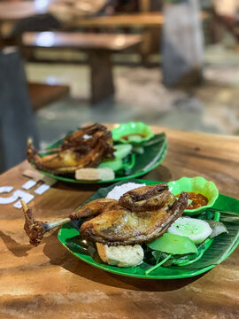 Ayam Tempong, Indonesian fried chicken served with rice, sambal, fresh vegetables, and tofu on banana leaf-lined plates, offering a traditional and spicy culinary experience.