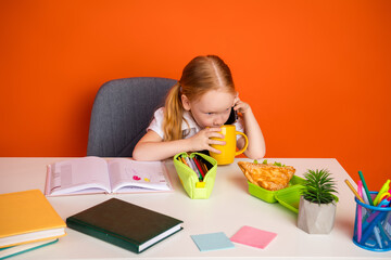 Young schoolgirl enjoying a meal while studying and speaking on the phone in a vivid orange setting...