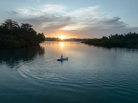 Aerial view of a man paddles a kayak on a tropical island with a sunset in the background. Slow motion video of a man enjoys the sunset while playing kayak