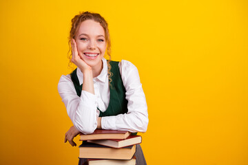 Cheerful student with study books against vibrant yellow background exemplifying learning,...