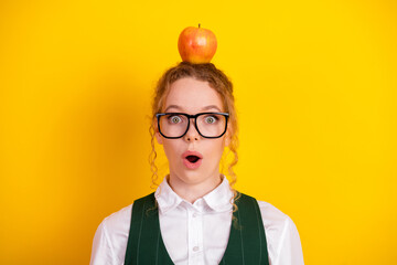 Surprised young student with an apple on her head against a bright yellow background, showcasing...
