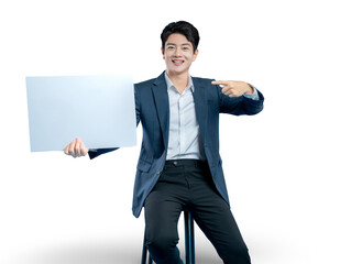 A cheerful Asian professional sits on a stool, holding a blank white board and pointing to it,...