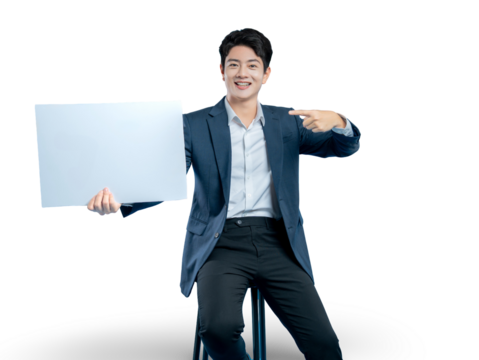 A cheerful Asian professional sits on a stool, holding a blank white board and pointing to it, ideal for showcasing information or an ad.

