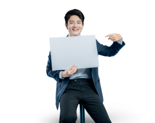 A smiling young man in a suit points to a blank white placard he is holding, perfect for drawing attention to an important message or feature.