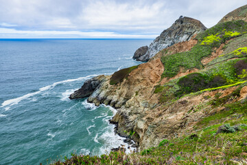 Dramatic ocean cliffs and lush coastal hills seen from Devils Bunker overlook, near Gray Whale Cove State Beach along Californias scenic Highway 1.