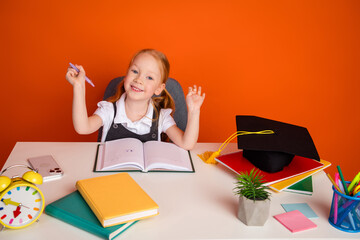 Adorable schoolgirl expressing excitement while studying at a desk surrounded by school supplies on...