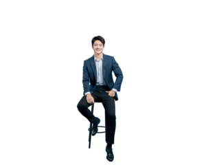 A relaxed and confident young Asian businessman sits on a stool with one hand in his pocket, smiling warmly at the camera.

