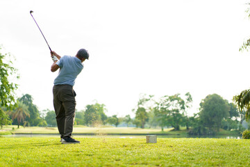 Elderly Asian man enjoying the morning round of golf in soft and warm sunlight.