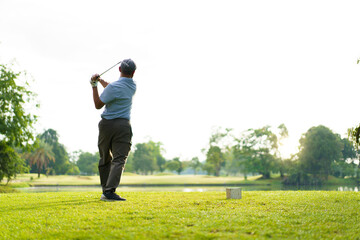 Elderly Asian man enjoying the morning round of golf in soft and warm sunlight.