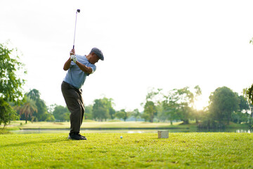 Elderly Asian man enjoying the morning round of golf in soft and warm sunlight.