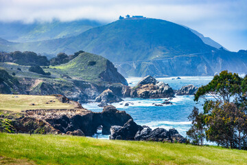 Scenic coastal view of Big Sur along Highway 1, California. Rugged cliffs, green hills, and the Pacific Ocean merge under soft clouds on the iconic Pacific Coast drive
