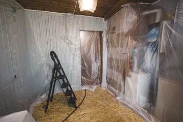A room covered with film during renovation, with a stepladder, ceiling light and protected...