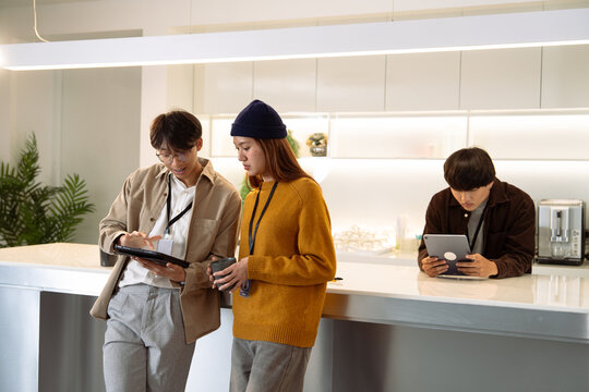 Three young adults engage with digital devices in a modern kitchen, showcasing collaboration and technology in a stylish workspace.