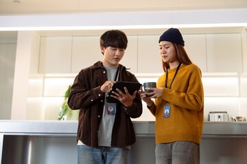 Two young adults engage in conversation while reviewing a tablet in a modern kitchen setting.