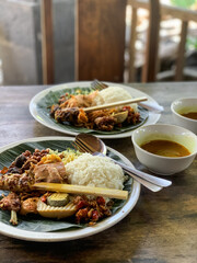 Nasi Campur is a Traditional Balinese rice dish served on a banana leaf with various side dishes,...