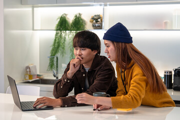 A young couple collaborates on a laptop in a modern kitchen, sharing ideas while enjoying a drink...