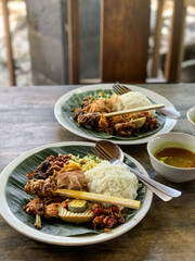 Nasi Campur is a Traditional Balinese rice dish served on a banana leaf with various side dishes,...