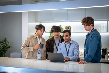 A group of young professionals collaborates around a laptop in a modern office setting, discussing...