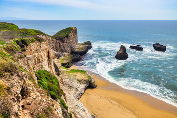 Scenic coastal cliffs and ocean waves near Davenport, California. Rugged rock formations rise above turquoise waters along the Pacific Coast, offering a breathtaking view from the trail