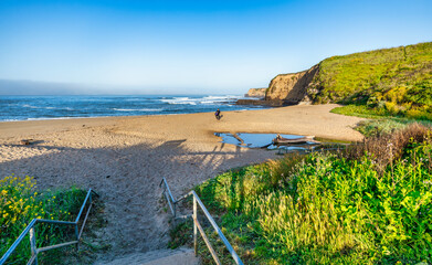 Beach access view from stairs near Highway 1, showing a peaceful sandy shore, ocean waves, and...