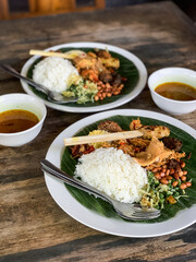 Nasi Campur is a Traditional Balinese rice dish served on a banana leaf with various side dishes,...