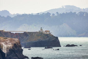 View of Point Bonita Lighthouse perched on a rocky cliff in Marin Headlands, California, captured from the Rodeo Beach Coastal Trail with the Pacific Ocean and misty hills in the background