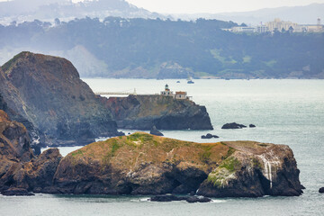 View of Point Bonita Lighthouse perched on a rocky cliff in Marin Headlands, California, captured from the Rodeo Beach Coastal Trail with the Pacific Ocean and misty hills in the background