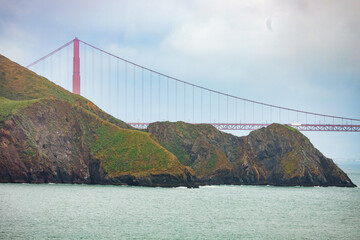 Close-up view of the Golden Gate Bridge rising behind rugged coastal cliffs of Marin Headlands,...