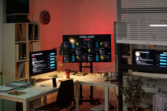 Empty office with multiple computer monitors displaying financial data and personal information, scam call center environment showing organized workstations and digital screens