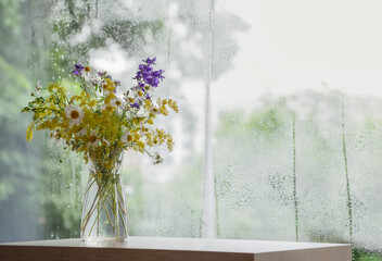 wildflowers in glass vase on background rainy window