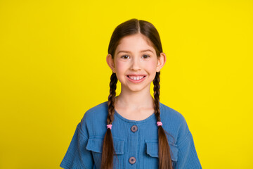 Smiling young girl wearing a blue outfit with braided hair posing in front of a vibrant yellow...