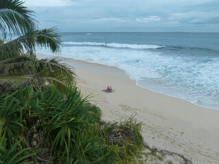 Aerial view of two friends enjoy the beauty of Indonesia's tropical beaches. Two young women sit together and chat on a beautiful tropical beach