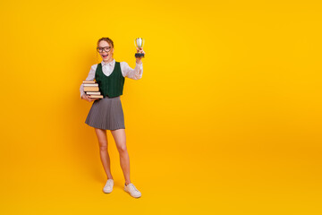 Confident student holding trophy and books with joy on cheerful yellow background celebrating...
