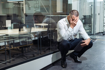Upset man in office clothes sitting alone with head in hands. Concept of job loss, stress and...