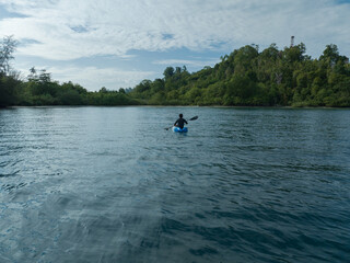 A man paddles a kayak on a tropical island. A man enjoying a sunny day while kayaking