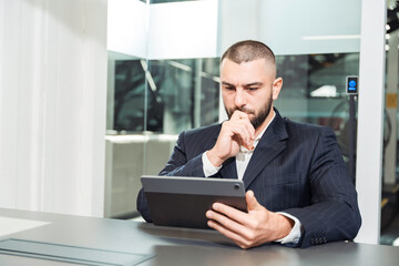Pensive man in business attire looking at tablet while thinking. Business planning, project...