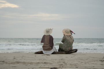 Two friends enjoy the beauty of Indonesia's tropical beaches. Two young women sit together and chat on a beautiful tropical beach
