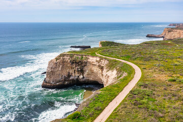 Coastal trail curves along dramatic sea cliffs near Davenport, California. Aerial view showcases a...