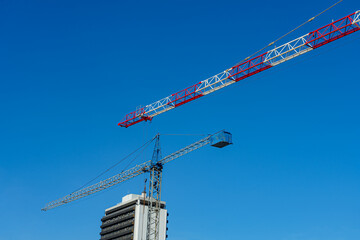 Two large construction cranes, one red and white, the other blue, dominate the skyline above a...